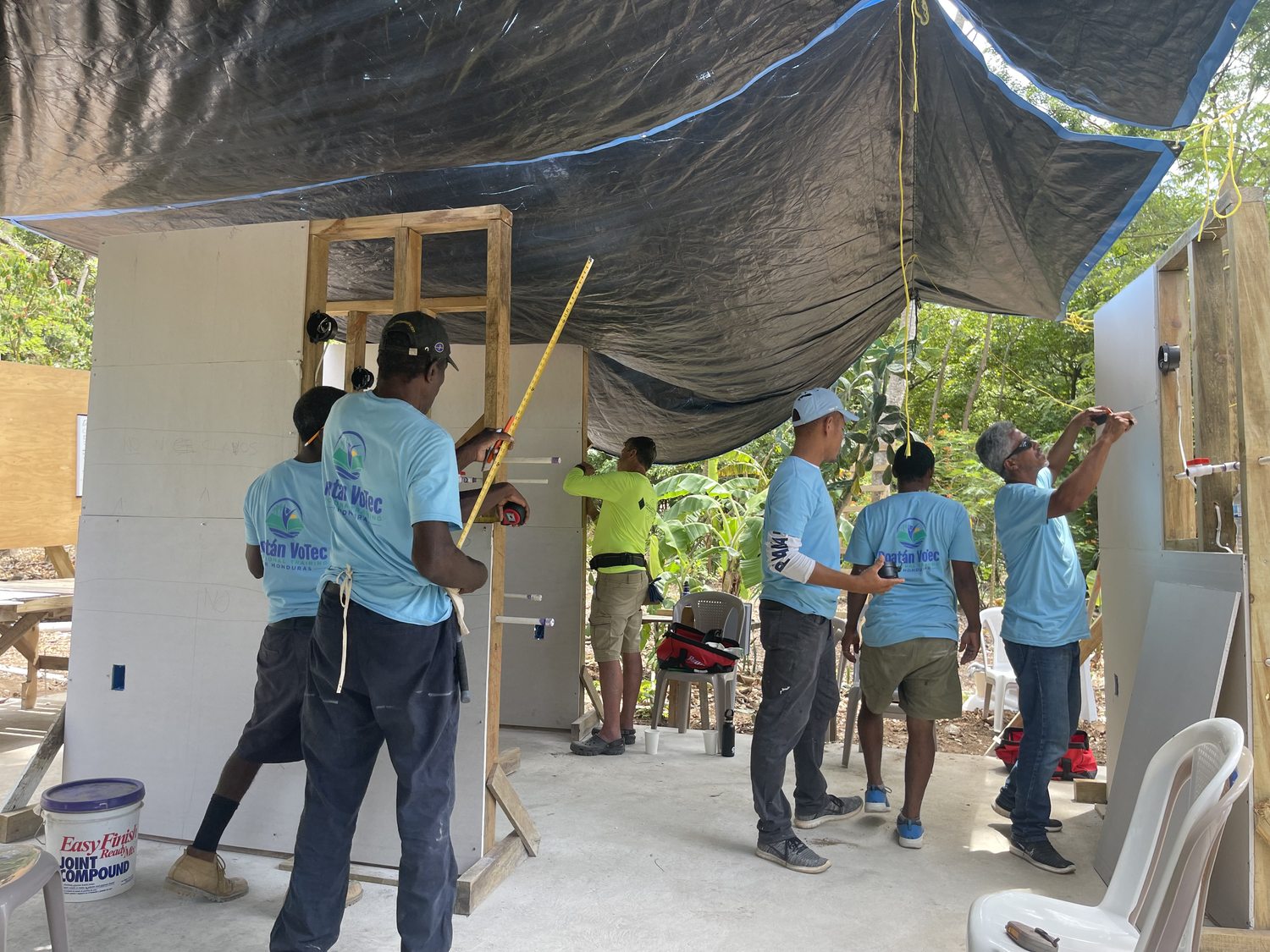 Students installing white drywall panels on the classroom exterior — RVT teal shirts throughout