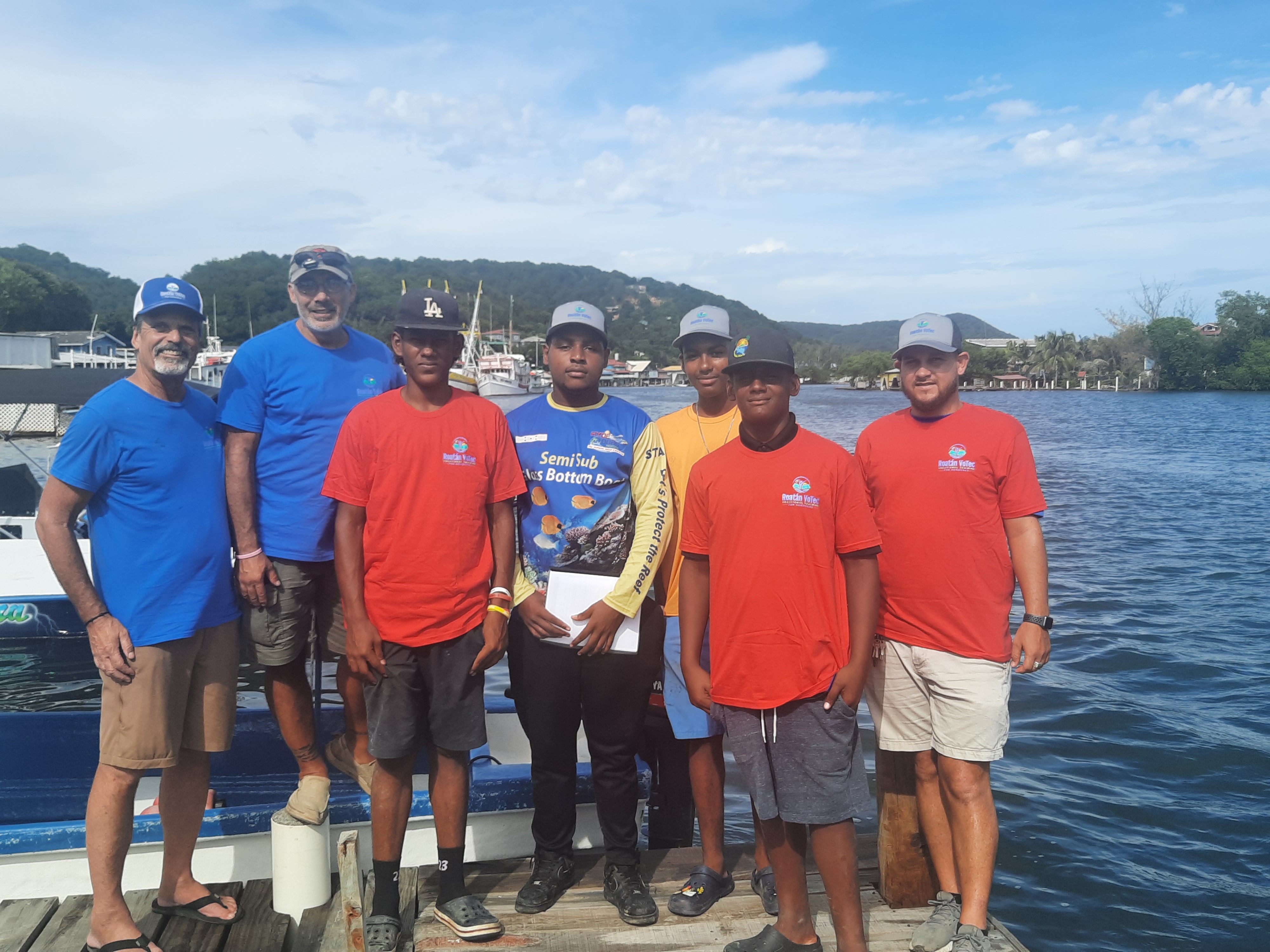 Outboard motor repair students graduating on the dock at Roatán — holding certificates by the water