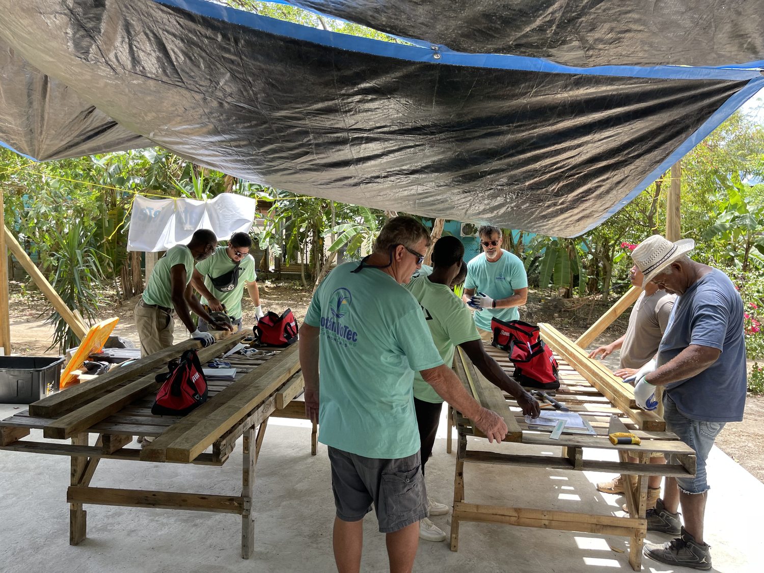 RVT students at outdoor workbenches measuring and assembling wall panels under a blue tarp